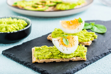 Appetizing sandwiches of crispy bread with avocado and boiled egg on slate.
