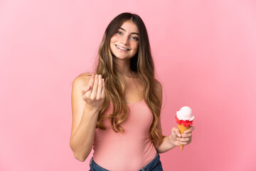 Obraz na płótnie Canvas Young caucasian woman with a cornet ice cream isolated on pink background inviting to come with hand. Happy that you came