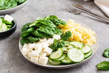 Bowl with pasta, cucumber, cheese and spinach on the table. Healthy vitamin nutrition