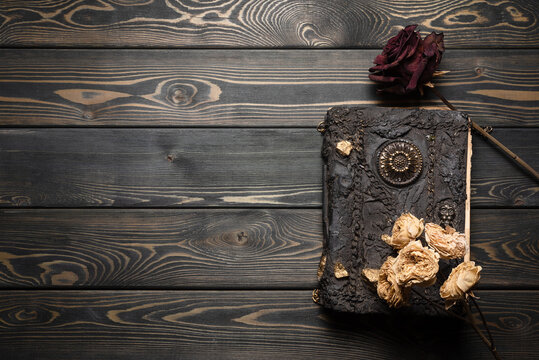 Ancient magic book and dry rose flowers on the old wooden table background with copy space. Witchcraft concept.