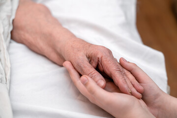 The grandson's hands hold the wrinkled hand of a sick elderly grandmother in a medical clinic. The concept of love and care. Slow movement