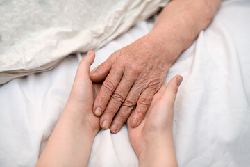 The grandson's hands hold the wrinkled hand of a sick elderly grandmother in a medical clinic. The...