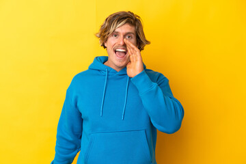 Handsome blonde man isolated on yellow background shouting with mouth wide open