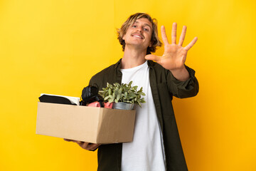 blonde man making a move while picking up a box full of things isolated on yellow background...