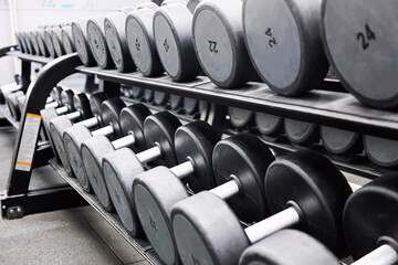 Obraz na płótnie Canvas Fitness sports concept. Black dumbbell set. Close up many metal dumbbells on rack in sport fitness center.
