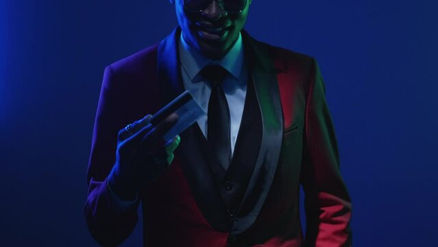 Bank service. Rich man. Luxury life. Cashless payment. Neon light unrecognizable confident vip client in elegant suit glasses showing credit card isolated on dark blue.
