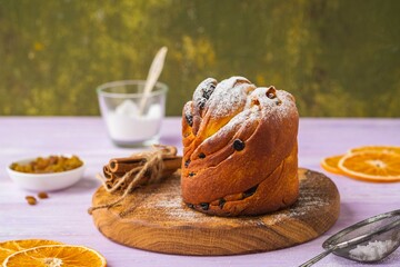 Kraffin (cruffin), yeast twisted cake with raisins sprinkled with powdered sugar on a wooden board on a purple wooden background.
