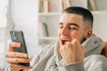 young teenager at home excited with mobile phone celebrating