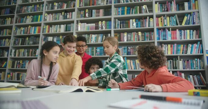 Kids draw with markers in sketchbook at table in library
