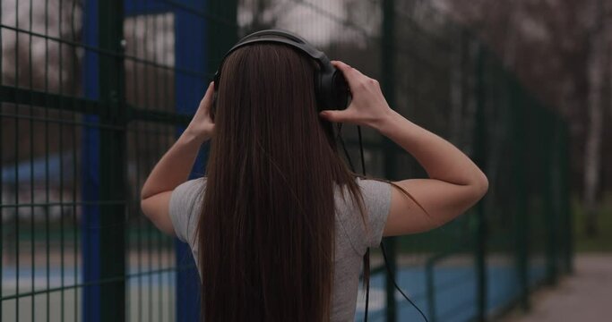 Cute girl walking in a park listening music in headphones, slow motion, back view