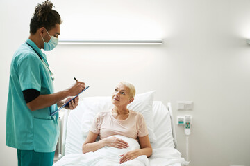 Doctor writing down diagnosis for pensioner in bed