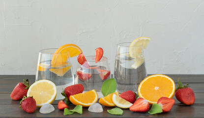 Three glasses with fresh lemonade made of fruits, oranges, lemons, strawberries and mint leaves lay on wooden table. Detoxing and healthy beverages, copyspace