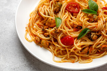 Spaghetti with mussels and tomato cherry sauce in white plate. Close up.
