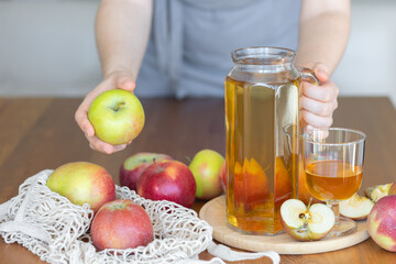 Young woman and fresh homemade organic apple juice or cider on a wooden table in a glass jug