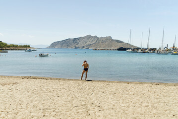 beautiful young woman in a bathing suit enjoys the summer holiday on the beach with yachts in the...