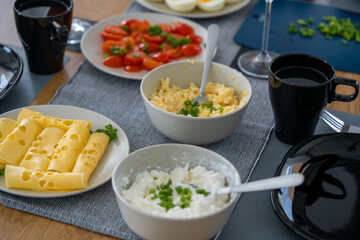 homemade breakfast, yellow cheese with holes, small sliced tomatoes, cottage cheese, egg paste, eggs, chives, tea, orange, carrot and grapefruit juice in wine glasses, black tableware.