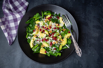 Avocado salad with spinach and pomegranate in a black plate on black background.