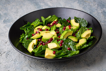 Avocado salad with spinach and pomegranate in a black plate on black background.