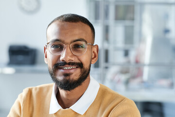 Portrait of smiling handsome young mixed race manager in eyeglasses sitting in contemporary office