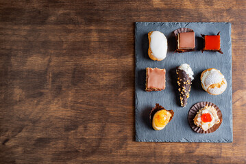 Various cakes on a rustic stone plate on a dark brown old wooden table.Copy space.