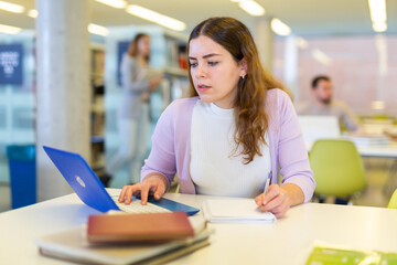Fototapeta premium Portrait of woman with laptop and book in public library