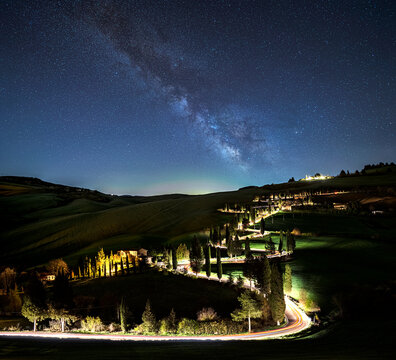 Curving cypress road at night with light trails and clear milky way sky near Monticchiello in the rolling hills of Tuscany, Italy