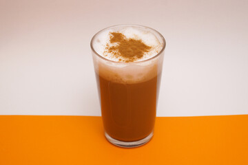 A glass of cappuccino with cinnamon. On an orange-white background.