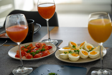 homemade breakfast, yellow cheese with holes, small sliced tomatoes, cottage cheese, egg paste, eggs, chives, tea, orange, carrot and grapefruit juice in wine glasses, black tableware.