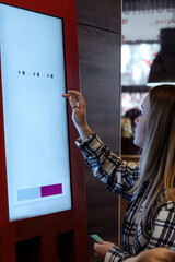 young beautiful woman chooses food and makes an order at the self-service terminal in a cafe