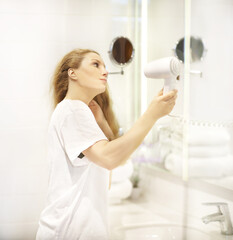 Fototapeta premium woman in the bathroom drying her hair with a hairdryer