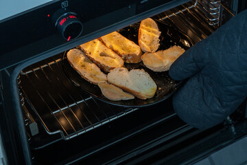 Baked toast with herbs in a preheated 250 degree Celsius oven pulled out with a black-gloved hand, safety at home.