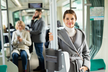 Fototapeta na wymiar Portrait of smiling brunette wearing stylish light overcoat during trip in public transport