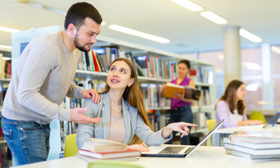 Obraz premium Male librarian helping focused adult student preparing to exam, bringing him books