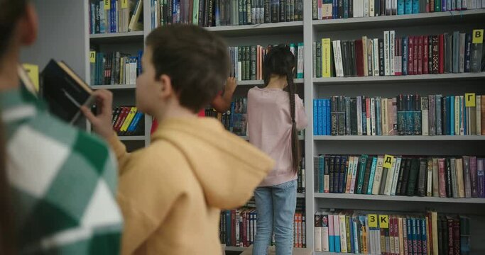 Multinational kids look for books on shelves in library