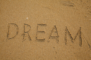 Fototapeta na wymiar Hand inscribed DREAM on the texture of beach sand.