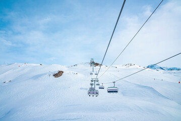 Ski lift moving over snow covered landscape. Chairlift on white mountain against blue sky. Idyllic view of alpine region during winter.