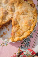 top down view of rhubarb pie with missing slice, pink tablecloth with blue roses	