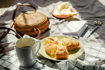 Morning breakfast in bed on blanket with tea, fruit and pie. Wicker bag and notebook. Light green color. Summer mood inspiration.