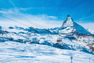Chairlift passing over snow covered landscape. Ski lift leading towards beautiful matterhorn mountain range. Scenic view of alps during winter.