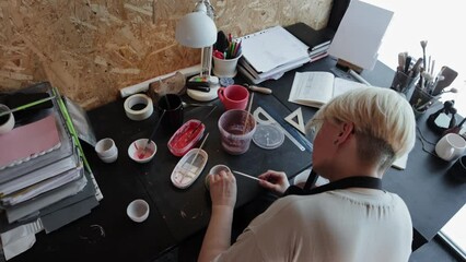 An elderly woman makes recesses on a ceramic mug