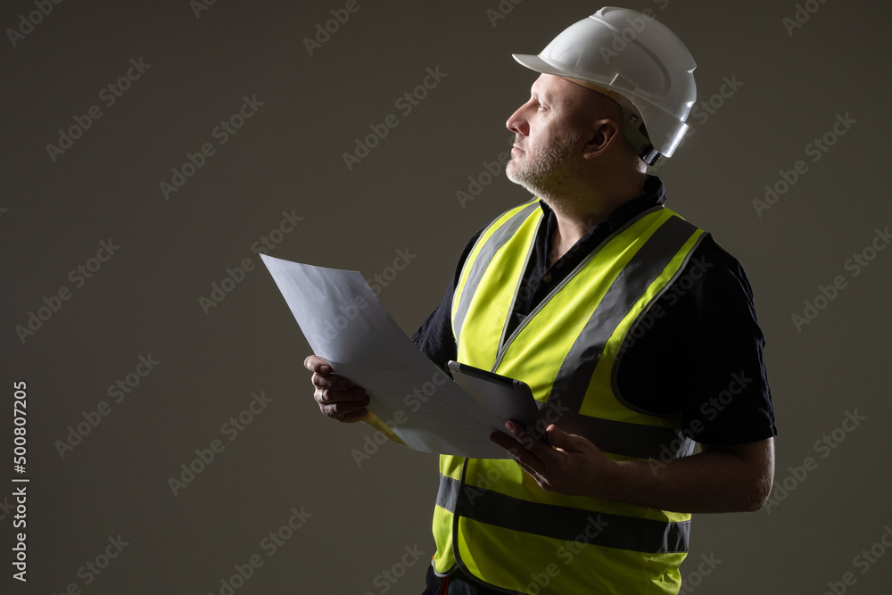 Poster builder looking up on dark background. man builder looks up. studio portrait of builder with sheet o