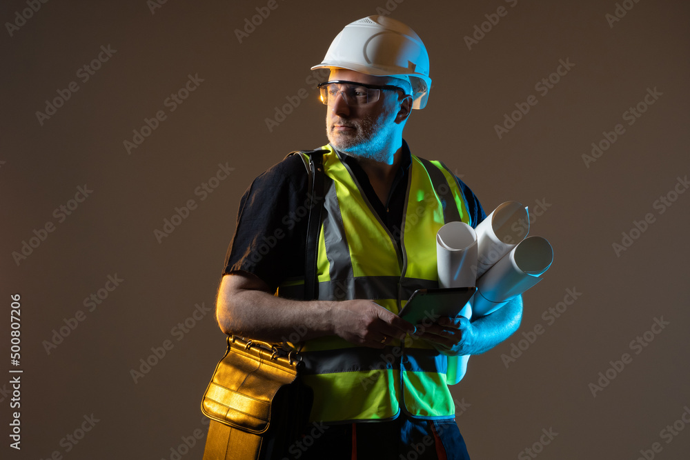 Poster Builders using digital tablet at construction site. Architect builder studio portrait. Portrait of an architect in the uniform of a builder. He looks away and thinks. Architect with electronic tablet