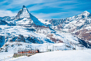 Fototapeta na wymiar View of red train climbing up to gornergrat station. Scenic view of matterhorn mountain against sky. Famous tourist place in alpine region.