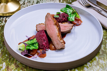 Duck breast with berry sauce and red cabbage on grey plate