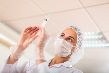 Female nurse or doctor wearing in face mask and medical uniform holding vial and syringe