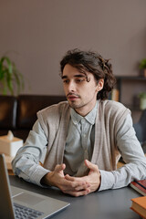 Obraz premium Vertical medium portrait of handsome young adult psychologist providing psychotherapy session for client on video call