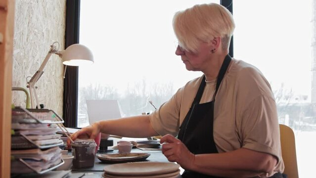 An elderly woman pours beige paint on the plate