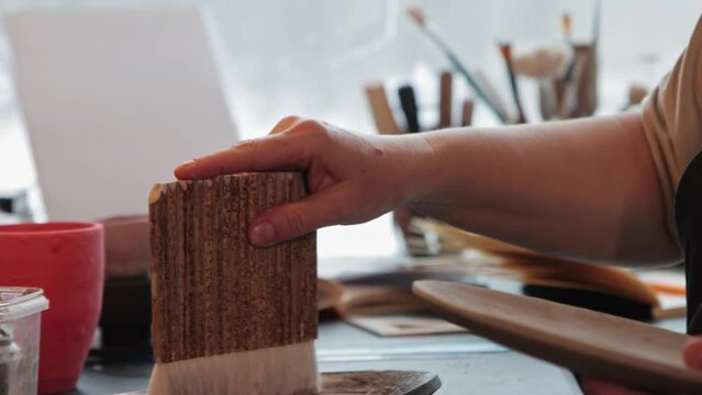 An elderly woman covers a clay plate with a special solution using a big brush