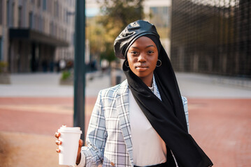 Serious black woman with takeaway coffee in modern district