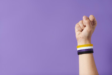 Raised fist of a person wearing a non binary flag bracelet. Gender identity diversity.